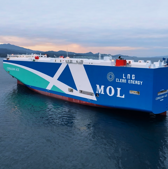 A large, blue and white cargo ship labeled "MOL" and "LNG Clean Energy" sails in calm waters at sunset, with distant mountains under a pink sky.