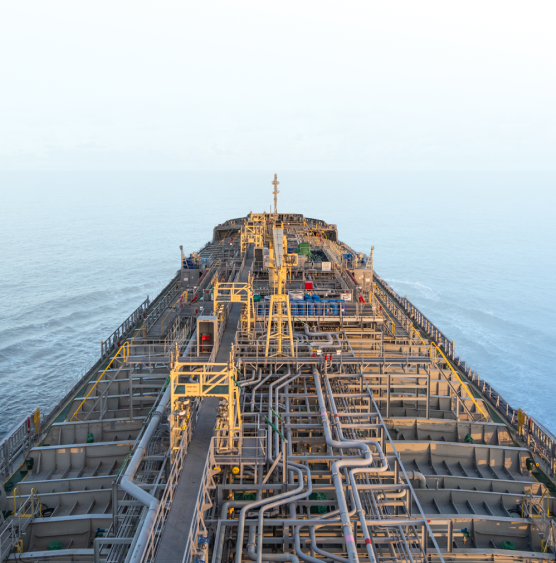 View from a ship's deck showing complex metal pipes and structures, extending towards the calm sea horizon under a clear sky, conveying industry and vastness.