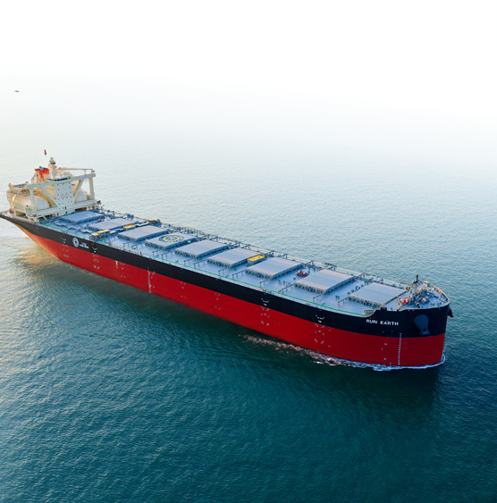 A large cargo ship with a red hull sails in calm blue waters under a clear sky. The vessel, marked "Run Earth," moves steadily, exuding strength.