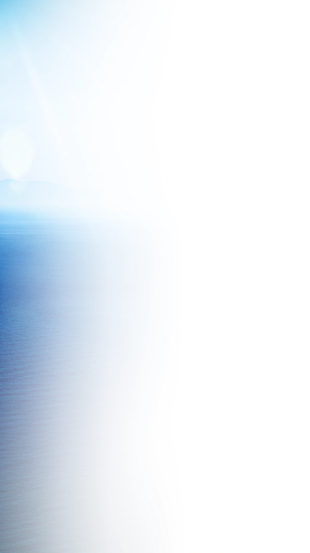 A serene seascape with calm blue water on the left fading into a bright white area on the right, with a soft, hazy horizon and a faint sun in the background.